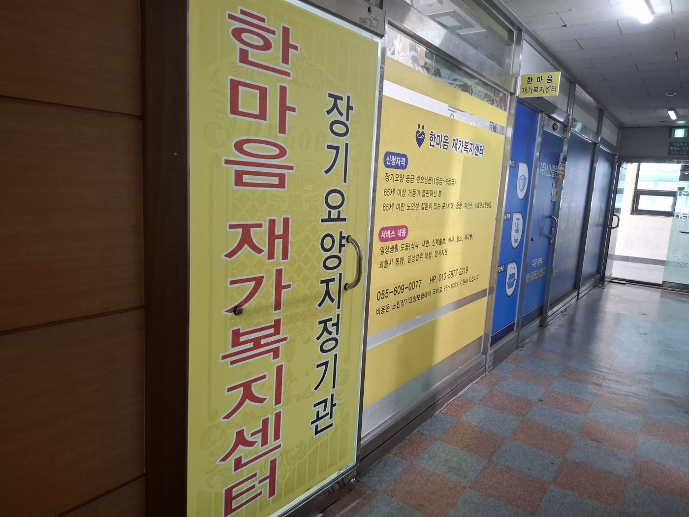 진한데파트 3층 복도. 왼쪽에 한마음재가복지센터 세로 간판과 노란 안내판이 붙은 유리문이 있고, 문 위에 센터 이름 표찰이 걸려 있다.